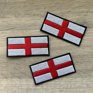 May include: Three embroidered patches featuring the flag of England. The patches are white with a red cross and a black border.