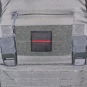 Könnte beinhalten: Eine graue taktische Weste mit einem schwarzen Patch mit einer dünnen roten Linie. Die Weste hat eine Reißverschlusstasche und verstellbare Träger mit schwarzen Schnallen, die mit "Viper" beschriftet sind.