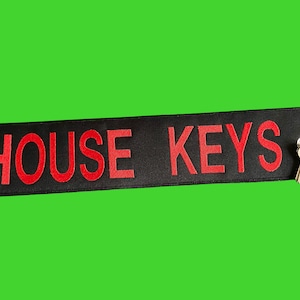 May include: Black fabric keychain with red embroidered text "HOUSE KEYS" and a silver key attached.