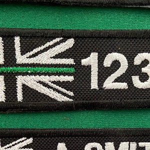 May include: Black and white embroidered patch with a Union Jack design and a green stripe across the middle. The number 1234 is embroidered in white on the right side of the patch.