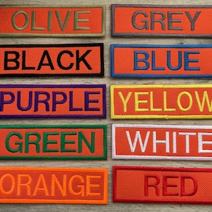 May include: A collection of ten rectangular embroidered patches with orange backgrounds, each featuring a different colour text: OLIVE, GREY, BLACK, BLUE, PURPLE, YELLOW, GREEN, WHITE, ORANGE, and RED. Each patch has a border matching its text colour.