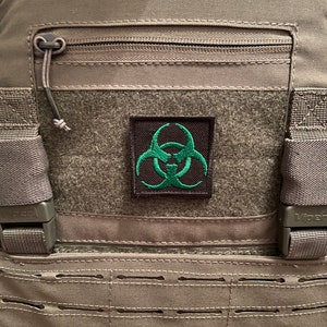 May include: A gray tactical vest with a black zippered pocket and a green biohazard symbol patch.