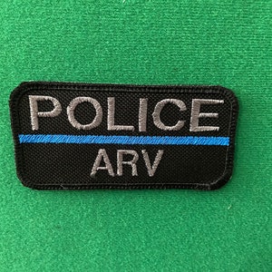 May include: Black and grey embroidered patch with a blue stripe. The patch reads "POLICE ARV".