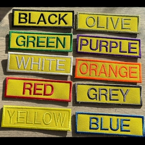 May include: A collection of ten rectangular embroidered patches with yellow backgrounds and coloured borders. Each patch features a different word embroidered in a matching colour: BLACK, OLIVE, GREEN, PURPLE, WHITE, ORANGE, RED, GREY, YELLOW, and BLUE.