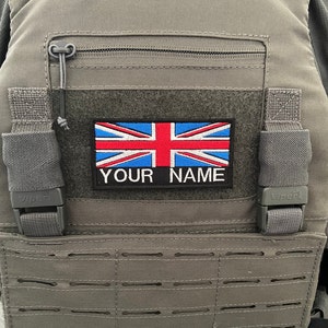 Peut inclure: Un gilet tactique gris avec un patch noir représentant le drapeau de l'Union Jack et le texte "YOUR NAME".