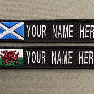 Peut inclure: Deux patchs brodés noirs avec du texte blanc qui dit "YOUR NAME HERE". Le patch de gauche présente un drapeau écossais bleu et blanc. Le patch de droite présente un dragon rouge sur un drapeau gallois vert et blanc.