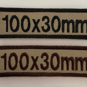 May include: Two beige fabric patches with black and brown stitching. The patches are rectangular and have the text "100x30mm" embroidered in black and brown thread.