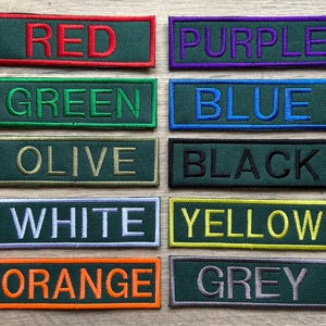 Puede incluir: Una colección de parches bordados en varios colores, cada uno con un nombre de color en mayúsculas. Los colores incluyen rojo, morado, verde, azul, oliva, negro, blanco, amarillo, naranja y gris, todos sobre un fondo verde oscuro.