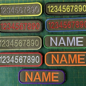 May include: Seven embroidered patches with different coloured borders. The patches are rectangular and have a green background. The first six patches have white numbers 1234567890 on them. The last three patches have the word "NAME" on them in white, orange, and white lettering.