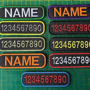 May include: Ten black fabric patches with white, yellow, orange, and red lettering. The patches have different color borders and read "NAME" and "1234567890".