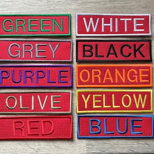 May include: A set of ten colour swatches, each with a different colour name embroidered on a red background. The colours are: green, white, grey, black, purple, orange, olive, yellow, red, and blue.
