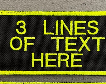 May include: A rectangular embroidered patch with a black fabric background and a bright neon yellow border. The patch features the embroidered neon yellow text "3 LINES OF TEXT HERE" centered in a bold, sans-serif font across three distinct lines.