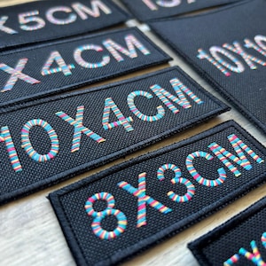 May include: A set of black fabric patches with colourful rainbow-like embroidery. The patches feature different size measurements in centimetres, including 2x5cm, 2x4cm, 10x4cm, 8x3cm, and 10x10cm.