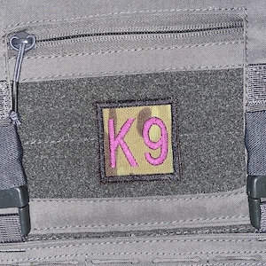May include: A gray tactical vest with a black zippered pocket and a black velcro patch with a pink "K9" embroidered on it.