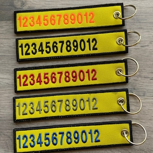 Może przedstawiać: Pięć żółtych breloków z czarnymi obwódkami i srebrnymi kółkami. Każdy brelok ma wyszyte liczby 123456789012 w różnych kolorach: pomarańczowym, czarnym, czerwonym, szarym i niebieskim.