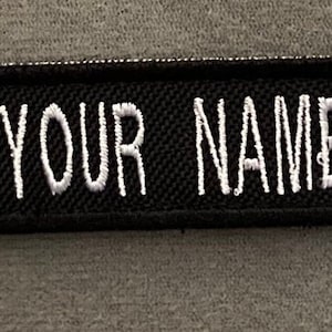 May include: Black and white embroidered name tag with the flag of the Faroe Islands on the left side and the text "YOUR NAME HERE" on the right side.
