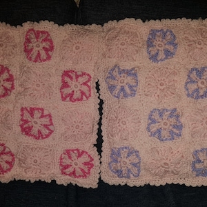 Puede incluir: Dos cuadrados de ganchillo con un patrón floral. Un cuadrado es rosa con un diseño de flores rosa oscuro, y el otro cuadrado es rosa claro con un diseño de flores morado claro.