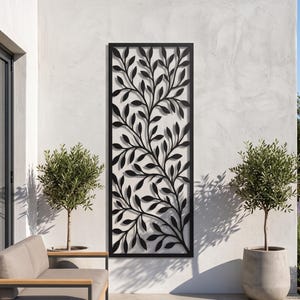Könnte beinhalten: Ein rechteckiges Wandpaneel aus schwarzem Metall mit einem lasergeschnittenen Design aus komplexen Zweigen und Blättern. Das Stück ist vertikal an einer hellen Außenwand montiert und zeigt ein detailliertes botanisches Muster mit Aussparungen.