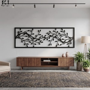 May include: A rectangular black metal wall art piece featuring a continuous vine design with numerous leaves. The artwork is framed in a thin black border and is mounted horizontally on a plain wall above a wooden media console unit.