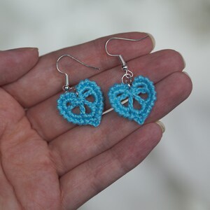 May include: A pair of blue crocheted heart-shaped earrings with silver hooks.