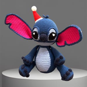 May include: A blue crocheted Stitch plush toy wearing a red and white Santa hat with pink ears.