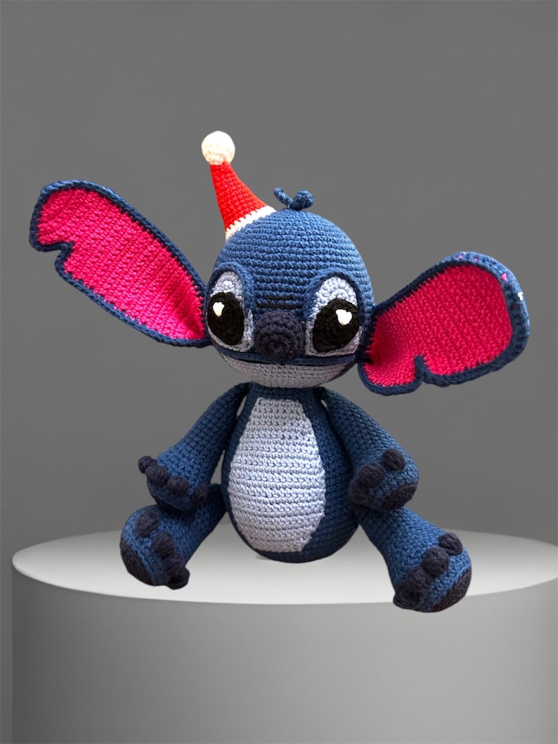May include: A blue crocheted Stitch plush toy wearing a red and white Santa hat with pink ears.