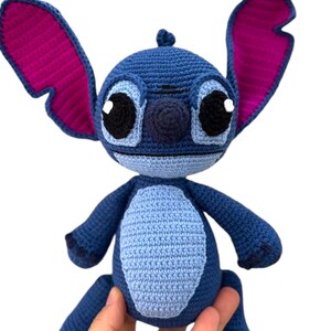 May include: Blue and purple crocheted Stitch plush toy with big eyes and a stitched-on smile.