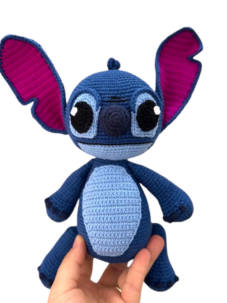 May include: Blue and purple crocheted Stitch plush toy with big eyes and a stitched-on smile.
