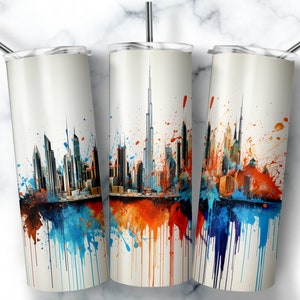 Puede incluir: Tres vasos de acero inoxidable con fondo blanco y un diseño de ciudad colorido. La ciudad está delineada en negro y presenta salpicaduras de pintura azul, naranja y roja.