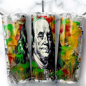May include: A stainless steel tumbler with a colorful abstract design featuring Benjamin Franklin's portrait and dollar bills. The design includes splashes of green, yellow, red, and orange paint.