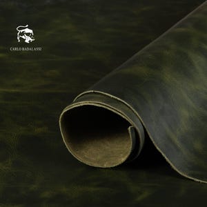 Könnte beinhalten: Eine Rolle dunkelgrünes Leder mit einem Used-Look-Finish. Das Leder ist teilweise ausgerollt und zeigt die Unterseite. Das Carlo Badalassi-Logo befindet sich in der oberen linken Ecke. Das Leder hat eine strukturierte Optik.