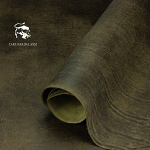 May include: A close-up of a rolled piece of dark green leather with a subtle, textured surface. The leather is rolled up and the edges are visible. The text "CARLO BADALASSI" is printed in white on the leather.