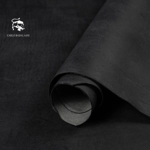 May include: A close-up of a rolled-up piece of black leather. The leather has a matte finish and a slightly textured surface. The Carlo Badalassi logo is visible in the upper left corner.