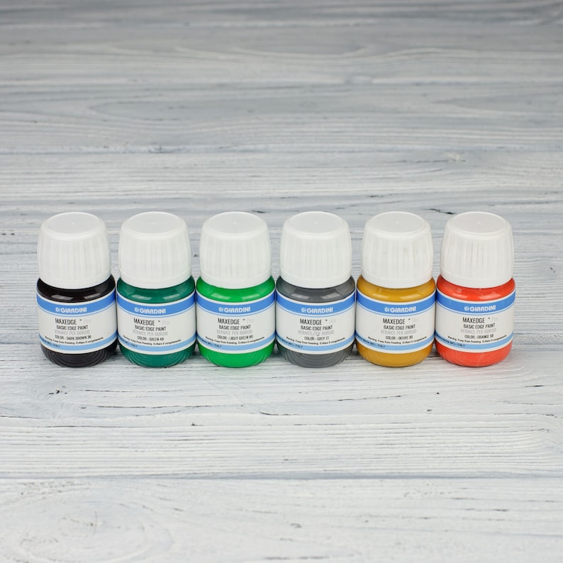 Puede incluir: Seis peque&ntilde;os frascos de pintura acr&iacute;lica en varios colores, incluyendo negro, verde, verde oscuro, gris, amarillo y naranja. Cada frasco tiene una etiqueta blanca con el texto "MAXEDGE BASIC COAT PAINT" y "GARDINI" impreso en ella.