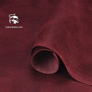 May include: A close-up of a deep burgundy leather hide rolled up. The leather has a textured surface and is soft and supple. The Carlo Badalassi logo is visible in the top left corner.