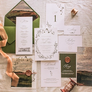May include: An assortment of wedding stationery, including invitations, menus, and thank you cards. The designs feature botanical illustrations and elegant calligraphy. A green envelope and a spool of thread are also present.