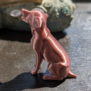 Labrador home decor figurine rose gold on a dark brown surface, in the background a greenish sculpture