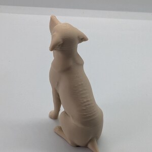 May include: A light beige, three-dimensional printed figurine of a dog sitting and looking upward. The sculpture features visible horizontal layer lines from the printing process, with pointed ears, a smooth back, and a short tail extending outward.