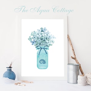 Peut inclure: Une peinture à l'aquarelle d'un bocal en verre bleu avec un ruban bleu et un motif de coquillage. Le bocal est rempli d'un bouquet de fleurs bleues et vertes. La peinture est encadrée et intitulée "The Aqua Cottage".