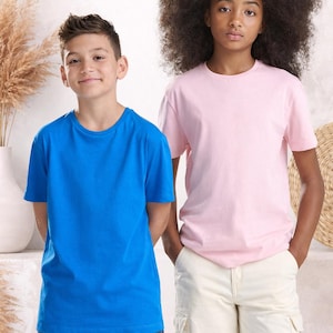 Op de afbeelding: Twee mensen dragen effen t-shirts. Eén persoon draagt een felblauw t-shirt en een spijkerbroek, de ander een lichtroze t-shirt en een witte cargobroek. De achtergrond is neutraal.