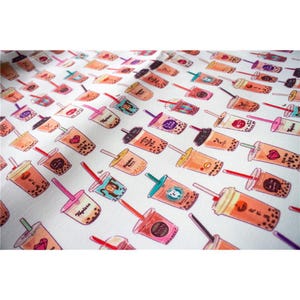 May include: A white fabric featuring a repeating pattern of various bubble tea drinks in shades of brown, orange, and pink. Each illustration depicts a plastic cup filled with tea, dark tapioca pearls at the bottom, and a colourful straw.