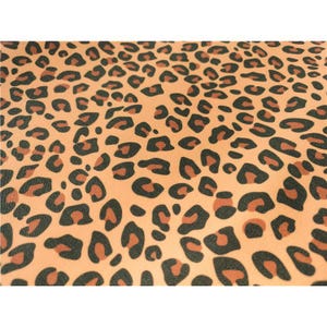 May include: A fabric featuring a repeating leopard print pattern with black and dark brown spots set against a light peach or soft orange background. The design covers the entire surface with a dense arrangement of organic, irregular shapes.