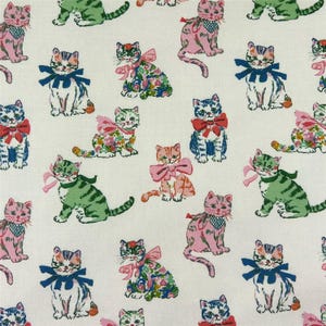 May include: A light-colored fabric featuring a repeating pattern of illustrated cats in various poses. The cats are depicted in shades of pink, green, and blue, many wearing bows or bandanas around their necks. The design includes floral accents.