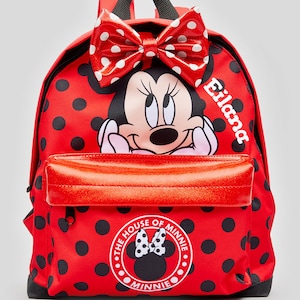 May include: Red polka dot backpack featuring a large Minnie Mouse image and a red bow. The backpack has a red zippered pocket and a white circle with the text "The House of Minnie" and a smaller Minnie Mouse image.