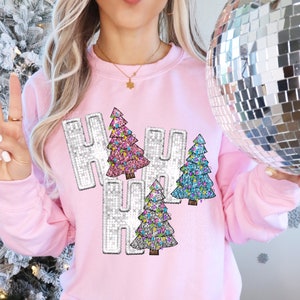 May include: A light pink sweatshirt with the word "HO HO HO" in silver sequins and colorful Christmas trees. The trees are decorated with pink, blue, and green lights. A disco ball is held in the background.