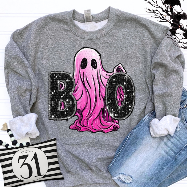 Op de afbeelding: Een grijs gem&ecirc;leerd sweatshirt met ronde hals en een afbeelding van een felroze geest tussen de zwarte letters B en O. De letters hebben een textuur met spikkels. Het sweatshirt wordt gecombineerd met een blauwe spijkerbroek.