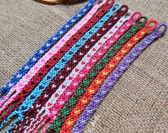 May include: A collection of colorful friendship bracelets with heart patterns. The bracelets are in various colors, including blue, pink, red, and green. The bracelets are handmade and have a woven design.