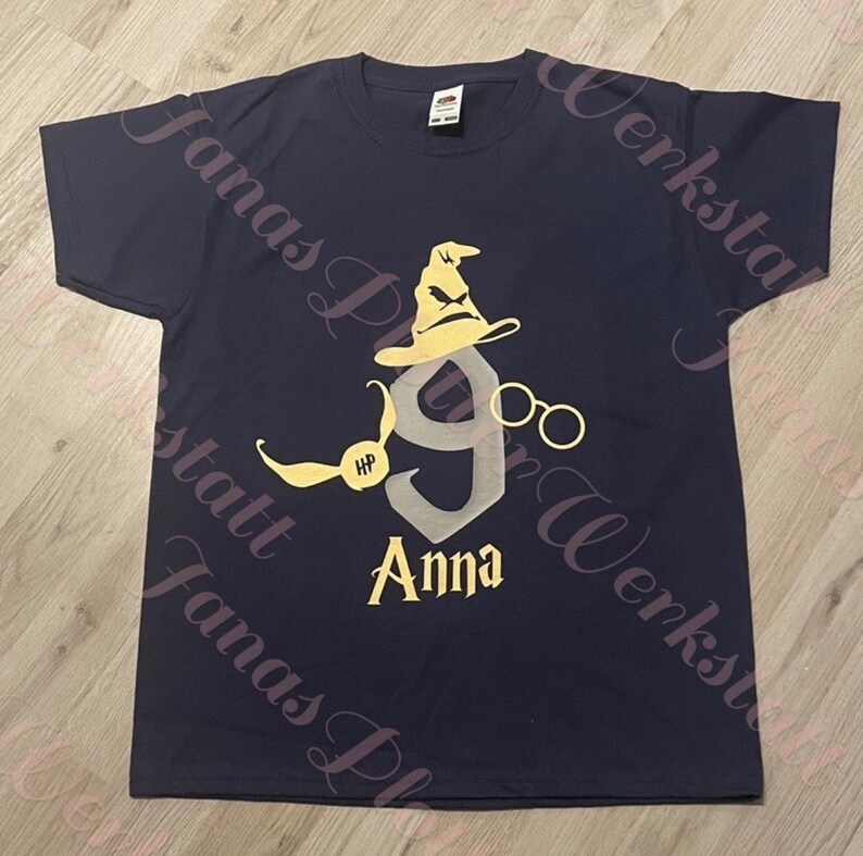 Pu&ograve; includere: Una maglietta blu navy con una grafica gialla e grigia di un cappello da mago, occhiali e il numero 9. Il testo "HP" e "Anna" sono anche sulla maglietta.