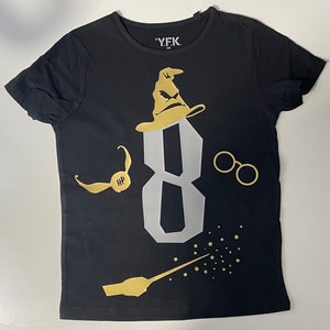Pu&ograve; includere: Maglietta nera con una grafica dorata del numero 8, un Cappello Parlante, un paio di occhiali, un Boccino d'Oro e una bacchetta magica con stelle. Il testo "Y.F.K." &egrave; sulla maglietta.