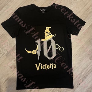 Könnte beinhalten: Schwarzes T-Shirt mit einer goldenen Grafik der Zahl 10, einem Zaubererhut, einer Brille und einem goldenen Schnatz. Der Text "Victoria" befindet sich unter der Zahl.